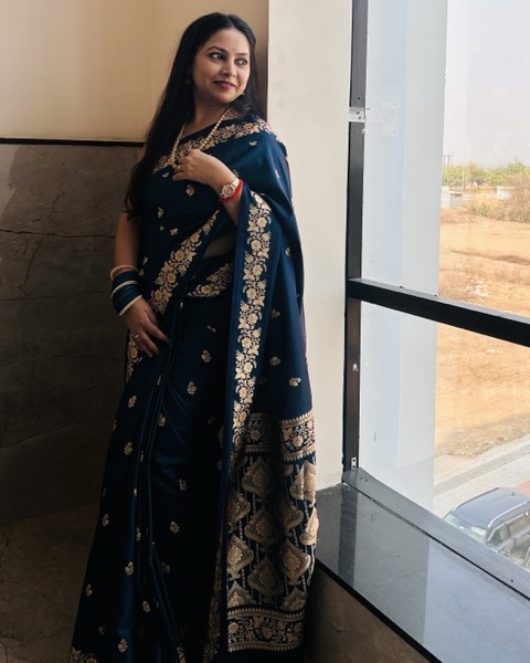 Standing by a window in a navy and gold saree