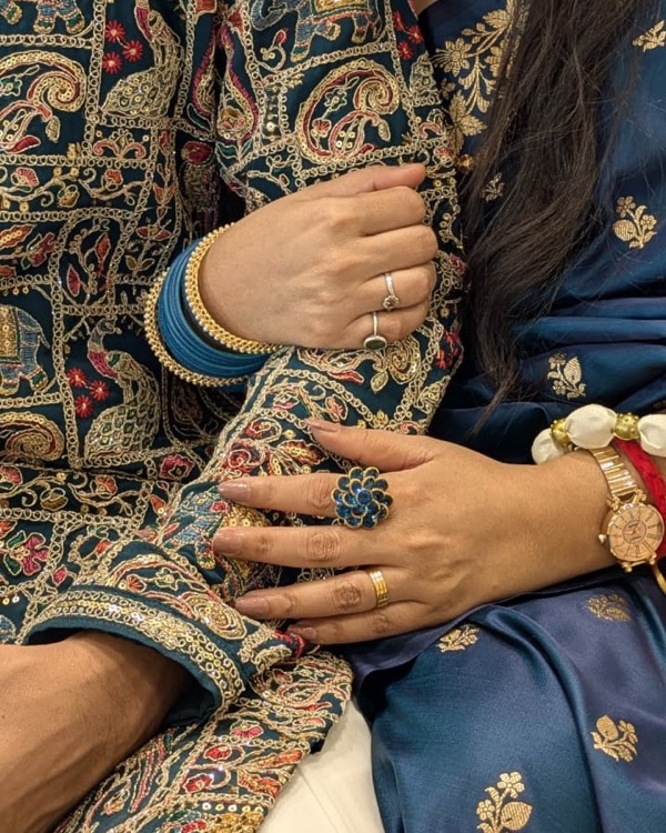 A close-up of our hands with the engagement rings, in embroidered and navy gold-motif outfits